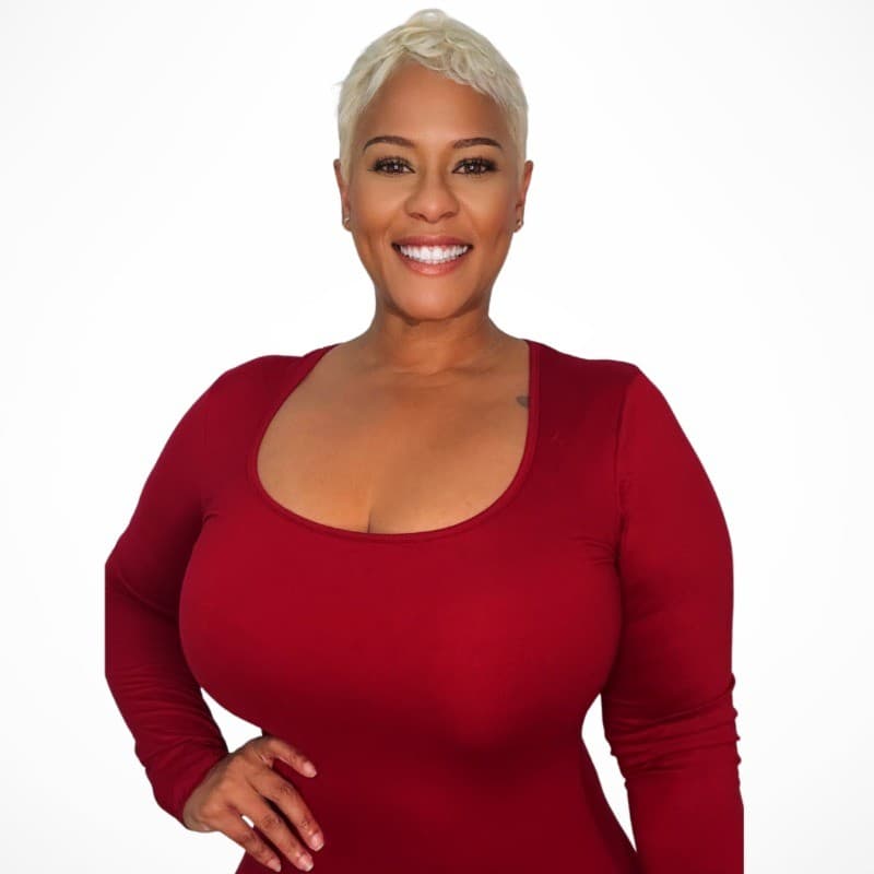 Smiling woman with short blonde hair wearing a red long-sleeved scoop neck top.